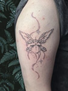 Arm Butterfly Tattoo by Isabella Roberts at Legendary Tattoos in Las Vegas Nevada. The butterfly tattoo is on the shoulder arm part and the background has contrasting greenery on the wall.