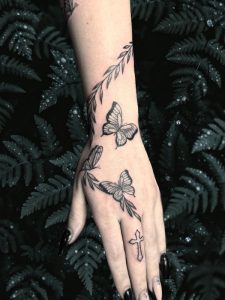 Hand Butterfly Tattoo by Isabella Roberts At Legendary Tattoos in Las Vegas, Nevada. In picture, you'll see a person's hand that's covered in butterfly tattoos with greenery nature tattoos spiraling up her arm.