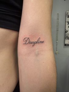 Discipline tattoo on inner forearm in elegant script style.