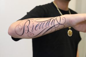 Elegant "Breathing" script tattoo on forearm, showcasing fine line work.