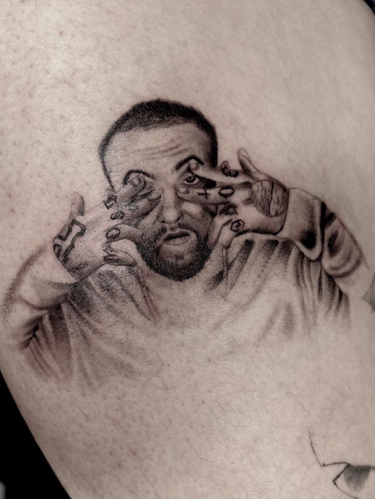 Black and grey portrait tattoo of Mac Miller by Henry Fuentes at Legendary Tattoos in Las Vegas, Nevada, showing him with hands framing his face and detailed finger tattoos.