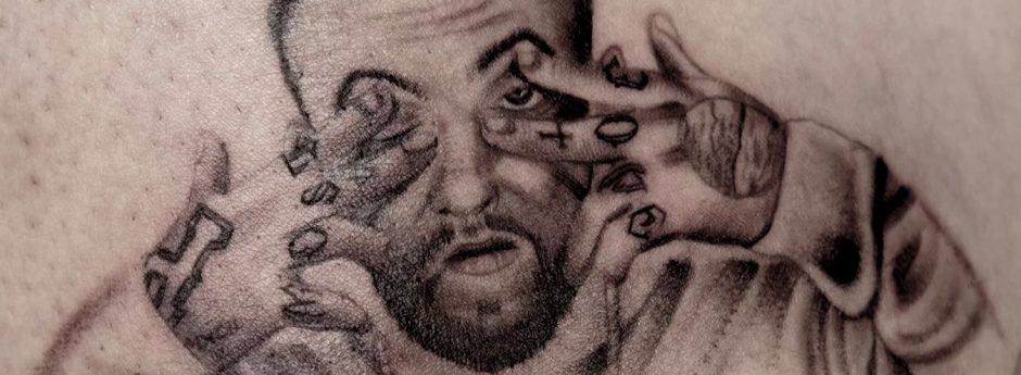 A black and grey portrait of a man with tattoos on his hands, making a face.